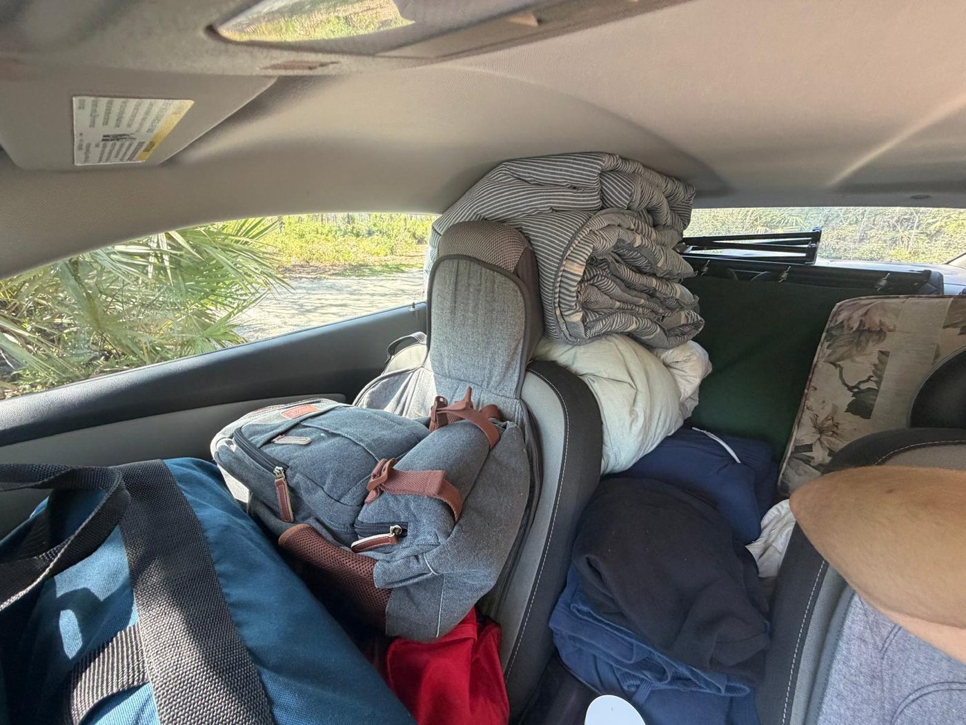 The interior of a car packed to the roof with bedding, clothing and belongings.
